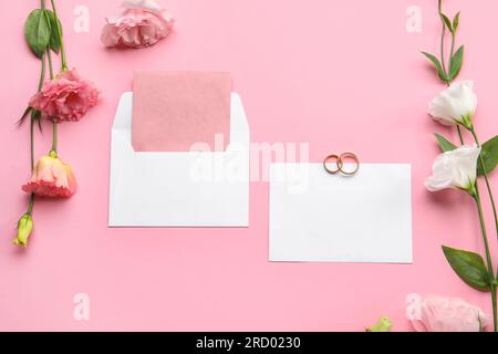 Composition avec des cartes vierges, enveloppe, anneaux de mariage et belles fleurs d'eustoma sur fond rose Banque D'Images