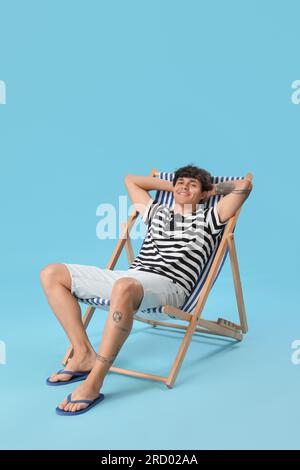 Jeune homme assis dans une chaise longue sur fond bleu Banque D'Images