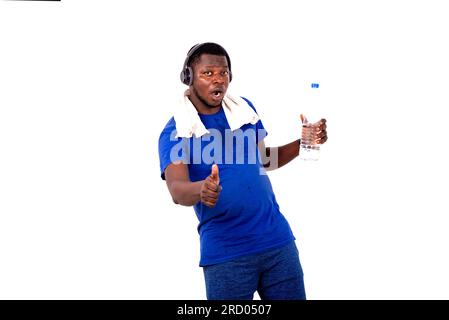 portrait d'un beau jeune homme sportif avec une serviette autour de son cou, portant un casque tenant une bouteille d'eau en plastique et montrant son pouce. Banque D'Images