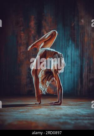 Jeune femme gymnaste s'étirant sur fond de mur sombre Banque D'Images