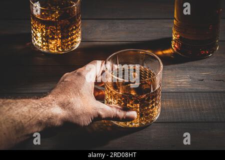 Main tenant un verre de whisky avec de la glace sur fond de table en bois. Gros plan. Banque D'Images