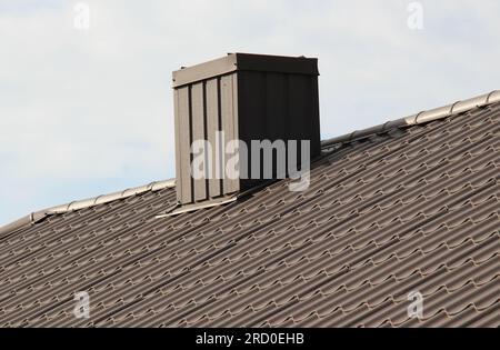 Une cheminée sur le toit d'une maison recouverte de tuiles métalliques ou d'un profilé métallique Banque D'Images