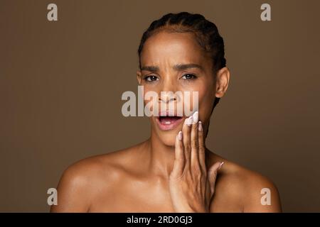 Problème dentaire. Femme noire d'âge moyen souffrant de maux de dents aigus, touchant le menton et fronçant les sourcils Banque D'Images