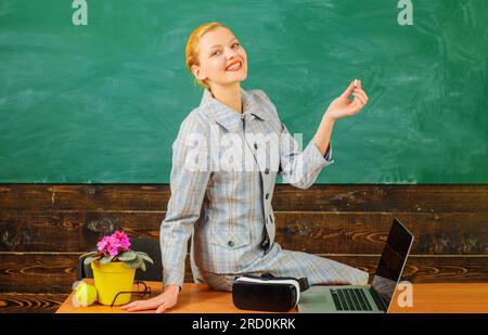 Enseignante souriante avec de la craie devant le tableau à la salle de classe. Retour à l'école. Éducation en ligne. Professeur souriant en costume assis à l'école Banque D'Images