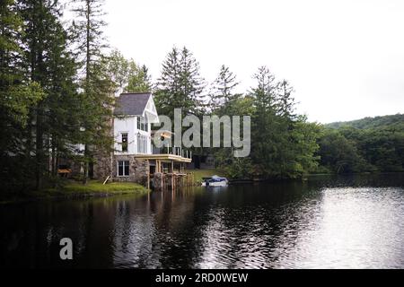 Un paysage avec une propriété au bord du lac entourée de forêts conduisant sur la route avec un arc-en-ciel à la fin et des gouttes de pluie sur le rebord de la fenêtre. Banque D'Images