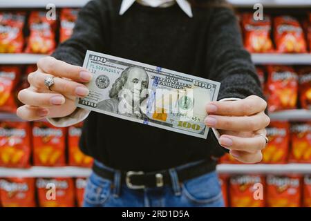 Femme tenant Un billet de 100 dollars au supermarché. Concept d'inflation et de hausse du Dollar en Argentine Banque D'Images