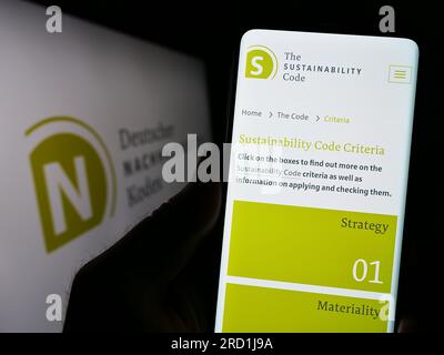 Personne tenant un téléphone portable avec la page web de Deutscher Nachhaltigkeitskodex (DNK) sur l'écran devant le logo. Concentrez-vous sur le centre de l'écran du téléphone. Banque D'Images