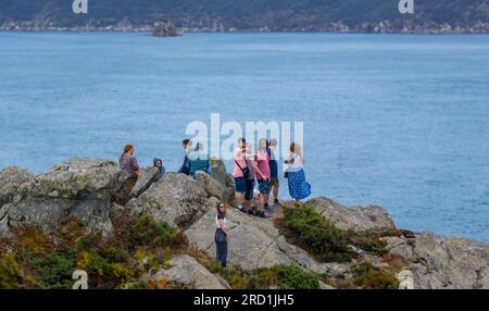 Groupe d'amis alpinistes et touristes au sommet d'une montagne rocheuse avec de la mousse et des lichens sous un ciel nuageux gris. En regardant l'océan et le hori Banque D'Images