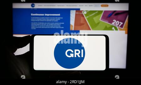 Personne détenant un téléphone portable avec le logo de la Global Reporting Initiative (GRI) à l'écran devant la page Web. Concentrez-vous sur l'affichage du téléphone. Banque D'Images
