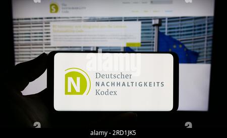 Personne tenant un smartphone avec le logo de Deutscher Nachhaltigkeitskodex (DNK) sur l'écran devant le site Web. Concentrez-vous sur l'affichage du téléphone. Banque D'Images