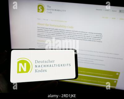 Personne tenant un téléphone portable avec le logo de Deutscher Nachhaltigkeitskodex (DNK) sur l'écran devant la page Web. Concentrez-vous sur l'affichage du téléphone. Banque D'Images