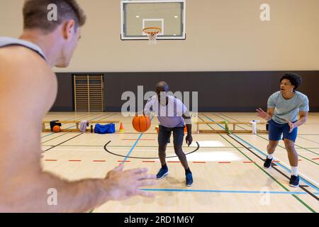 Divers joueurs de basket-ball masculins portant des vêtements de sport gris et jouant au basket-ball au gymnase Banque D'Images