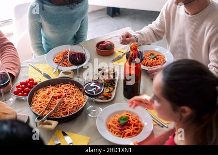 Gros plan de jeunes amis avec des fourchettes debout près de la table servie avec des pâtes maison Banque D'Images