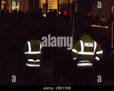 Lueur des costumes des policiers alors que l'obscurité tombe. Des officiers de la police du Grand Manchester font la queue pour regarder les fans de football dans les bars d'un Exchange Square animé, au centre de Manchester, au Royaume-Uni, avant la ronde Manchester United vs Ajax UEFA Europa League de 32, qui se tiendra à Old Trafford, le jeudi 23 février 2012. L'atmosphère est tendue. MUFC a continué à perdre le match, mais ils ont toujours avancé sur Aggregate pour réserver un match nul de la Ligue Europa-16. Quinze personnes ont été arrêtées après qu'un bar a été vandalisé sur Arundel Street, Manchester, dans des troubles avant la deuxième manche de l'Europa League. Banque D'Images