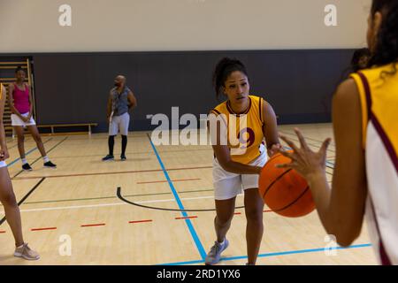 Joueurs de basket-ball biracial focalisés avec entraîneur masculin jouant au basket-ball à la salle de gym Banque D'Images