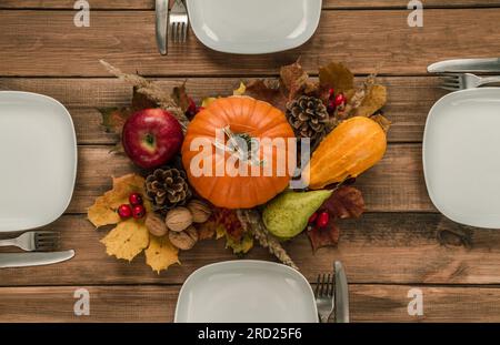 Table rustique en bois pour le dîner de Thanksgiving. Composition de pose plate d'automne ou d'automne. Assiettes, couverts, citrouilles, cônes, pomme, poire, noix, rose musquée, feuilles. Banque D'Images