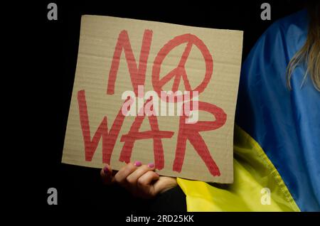 Femme tenant drapeau ukrainien et pancarte No War avec signe de paix. Manifestation contre l'invasion russe de l'Ukraine. Attaque russe, manifestation anti-guerre. Banque D'Images