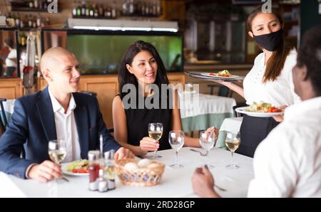 busboy femelle positif dans l'ordre de sectionnement de masque à des amis dans restaurante moderne Banque D'Images