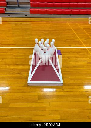Un jeu de trous de maïs maison avec dix quilles de bowling sur le dessus dans une salle de gym d'école secondaire. Banque D'Images