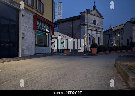 Chaussée devant un groupe de bâtiments et vitrines dans une ville italienne au crépuscule Banque D'Images