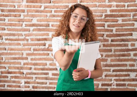 Jeune femme caucasienne tenant un cahier d'art souriant joyeux offrant main de paume donnant assistance et acceptation. Banque D'Images