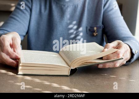 Gros plan d'une femme âgée assise à table lisant un livre de fiction. Vieille dame passant du temps à lire un livre de papier à la maison. La lecture aide à entraîner brai Banque D'Images