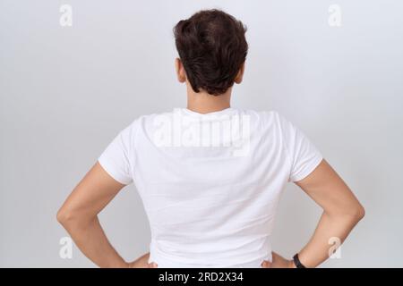 Jeune homme non binaire portant un t-shirt blanc décontracté debout en arrière regardant loin avec les bras sur le corps Banque D'Images