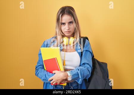 Jeune femme blonde portant un sac à dos étudiant et tenant des livres semblant somnolents et fatigués, épuisés pour la fatigue et la gueule de bois, les yeux paresseux le matin. Banque D'Images