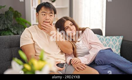 Homme et femme couple regardant la télévision avec une expression sérieuse à la maison Banque D'Images