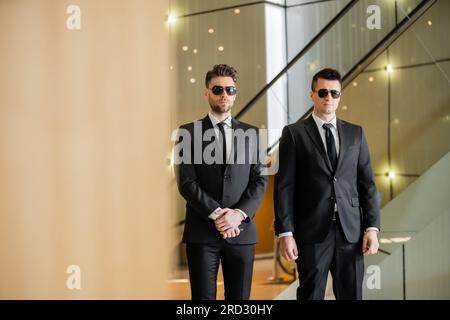 gardes de sécurité, deux beaux hommes en tenue formelle et lunettes de soleil, gardes du corps en service, mesures de sécurité, vigilance, costumes et cravates noirs, sécurité privée Banque D'Images