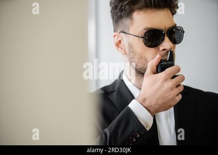 surveillance, garde du corps communiquant par talkie-walkie, homme en lunettes de soleil et costume avec cravate, sécurité de l'hôtel, gestion de la sécurité, garde en uniforme o Banque D'Images