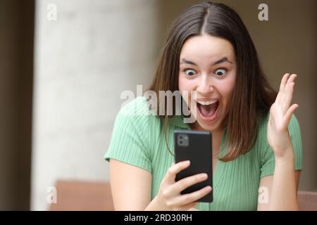 Femme excitée vérifiant le contenu incroyable sur le téléphone dans la rue Banque D'Images
