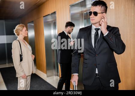 bodyguard service, protection personnelle, femme blonde en tenue formelle debout près des ascenseurs, personnel de sécurité protégeant la femme d'affaires réussie dans Banque D'Images