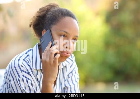 Femme noire impatiente se plaignant de parler au téléphone dans un parc Banque D'Images