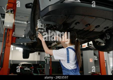 Femme auto mécanicien fixant le train de roulement de la voiture à la station-service Banque D'Images
