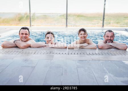 Deux couples mariés discutent et profitent d'une piscine extérieure. Les amis rient et se détendent dans l'eau tourbillonnante. Les jeunes se détendent dans un spa ou un hôtel. Banque D'Images