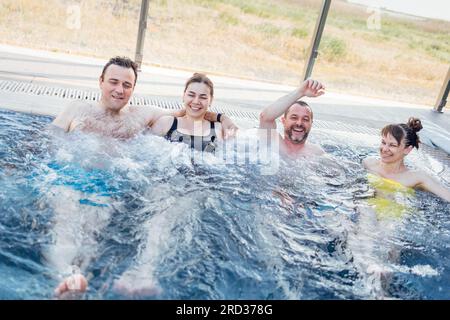 Deux couples mariés discutent et profitent d'une piscine extérieure. Les amis rient et se détendent dans l'eau tourbillonnante. Les jeunes se détendent dans un spa ou un hôtel. Banque D'Images