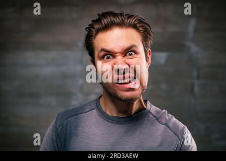 Portrait émotionnel jeune homme fou sur fond de mur gris Banque D'Images