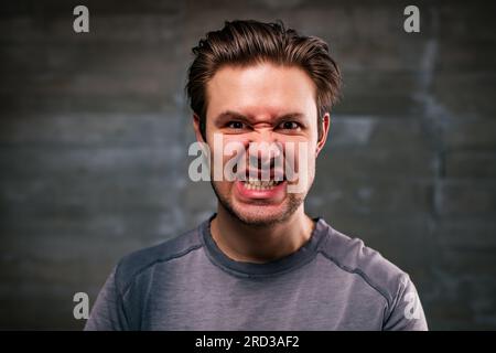 Portrait en colère de jeune homme sur fond de mur gris Banque D'Images