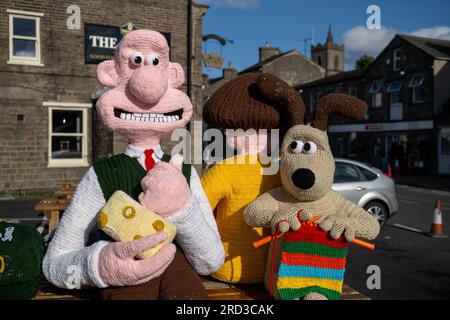 Hawes, North Yorkshire. 17 juillet 2023. Les Hawes Yarnbombers, un groupe local de tricoteuses extrêmes, ont dévoilé leur dernière création dans la ville marchande de Hawes, au cœur des Yorkshire Dales. Les personnages tricotés plus grands que nature de Wallace et Gromit, ainsi que d'autres personnages de la série, prennent plusieurs bancs, et voient Wallace avec un gros morceau de fromage Wensleydale, qui est son préféré, et est célèbre dans la Wensleydale Creamery basée à Hawes. Les dons pour les œuvres sont versés au Yorkshire Air Ambulance Service. Crédit : Wayne HUTCHINSON/Alamy Live News Banque D'Images