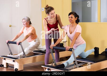 Femme hispanique pratiquant le pilates sur réformateur avec une jeune femme entraîneur Banque D'Images