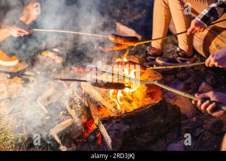 Frire des saucisses sur un feu dans la nature le soir. Cuisine extérieure. Banque D'Images