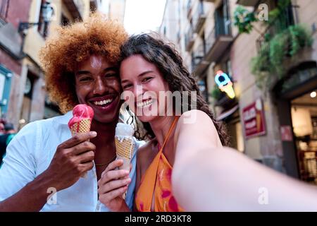 couple multiethnique profitant de l'été dans la ville et prenant selfie tout en mangeant de la crème glacée Banque D'Images