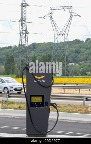 FRANCE, station de recharge rapide pour véhicule électrique à la station de carburant Dyneff sur l'autoroute, derrière le champ de tournesol et poteau de transmission de puissance / FRANKREICH, Fastned Stromladestation für Elektrofahrzeuge an Dyneff Tankstelle an der Autobahn, hintergrund Sonnenblume Feld Banque D'Images