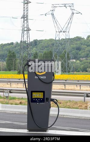 FRANCE, station de recharge rapide pour véhicule électrique à la station de carburant Dyneff sur l'autoroute, derrière le champ de tournesol et poteau de transmission de puissance / FRANKREICH, Fastned Stromladestation für Elektrofahrzeuge an Dyneff Tankstelle an der Autobahn, hintergrund Sonnenblume Feld Banque D'Images