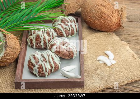 Petits pains à choux profiteroles à la crème de coco servis dans un style tropical. Feuilles de palmier, dessert sucré et sain, pose plate, espace de copie Banque D'Images