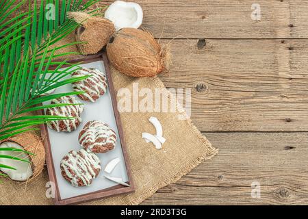 Petits pains à choux profiteroles à la crème de coco servis dans un style tropical. Feuilles de palmier, dessert sain sucré, plat, vue de dessus Banque D'Images