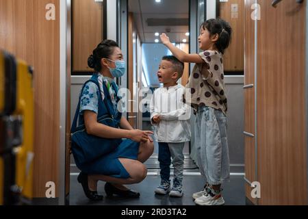 (230718) -- MENGLA, 18 juillet 2023 (Xinhua) -- Yi Bofeng (1e L) interagit avec des passagers à bord du train D887 le 16 juillet 2023. Yi Bofeng est originaire du comté de Mengla dans la province du Yunnan. Après avoir obtenu son diplôme de major laotien dans un collège technique de la capitale provinciale Kunming en 2020, elle a été recrutée comme hôtesse de train dans China Railway Kunming Bureau Group Co., Ltd Le chemin de fer Chine-Laos, un projet historique de coopération de haute qualité ceinture et route, a commencé ses opérations en décembre 2021. Yi était à bord du premier train du chemin de fer, témoin du moment historique de l'exploitation ferroviaire. Banque D'Images