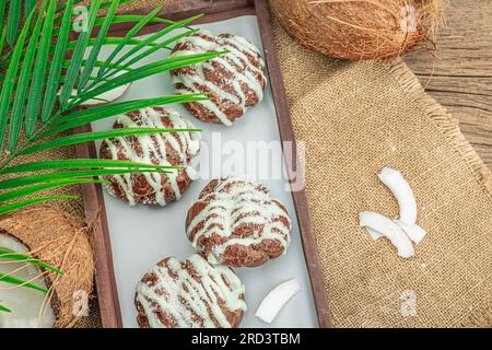 Petits pains à choux profiteroles à la crème de coco servis dans un style tropical. Feuilles de palmier, dessert sain sucré, plat, vue de dessus Banque D'Images