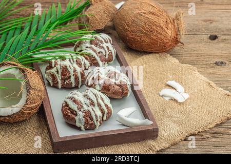 Petits pains à choux profiteroles à la crème de coco servis dans un style tropical. Feuilles de palmier, dessert sucré et sain, pose plate, espace de copie Banque D'Images